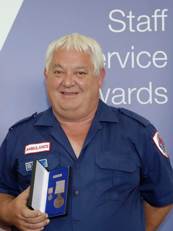 A man in Ambulance Victoria uniform smiles at the camera holding an award.