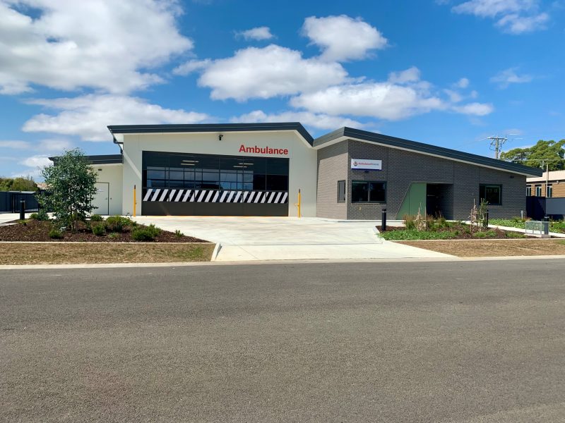 A modern, large ambulance branch on a sunny day. There are two sections to the building - a garage and a main building.