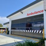 An ambulance branch garage door closed. An ambulance is parked next to it. The sky is blue.