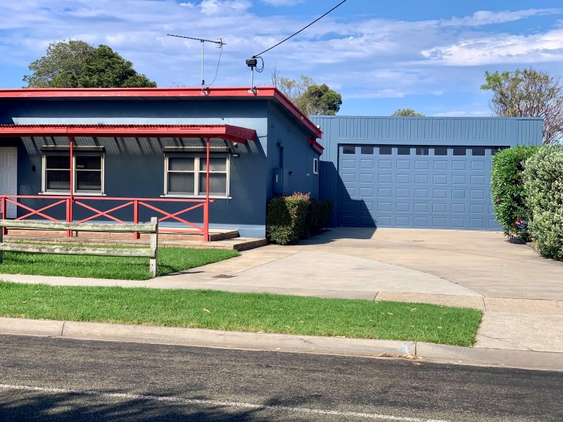 A small building with blue walls and red trim, and what looks like a two-vehicle garage.